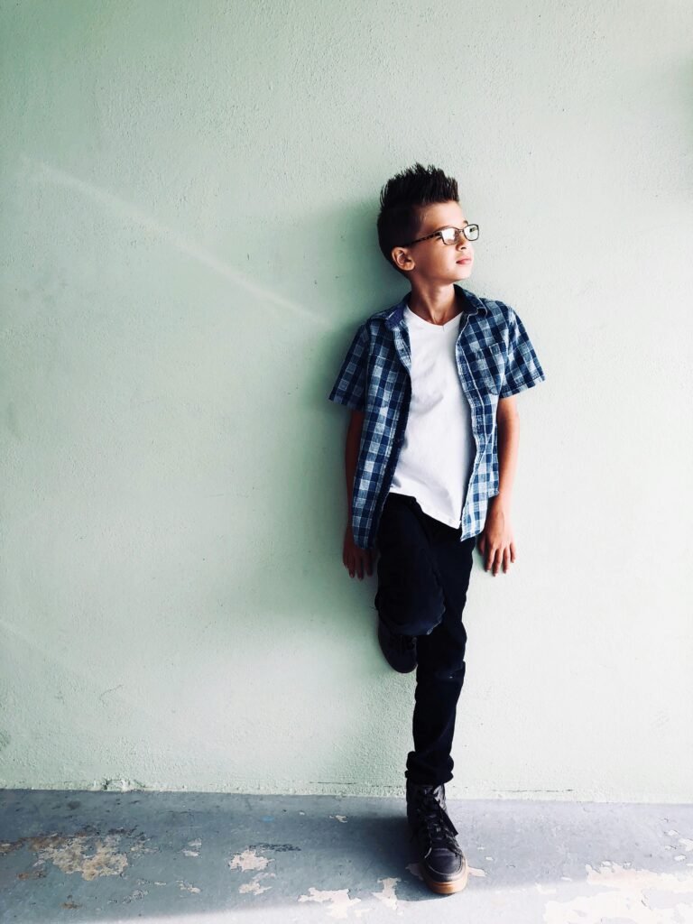 pexels-photo-969373-969373 Fashionable young boy wearing plaid shirt, posing against a light wall, exuding stylish confidence.